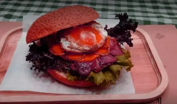 همبرگر بزرگ و خوشرنگ رستوران نیمکت با نان قرمز، تخم مرغ نیمرو، بیکن و کاهو تازه، سرو شده در سینی چوبی.