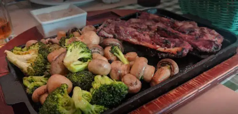 تصویری جذاب از بشقاب استیک و کباب لذیذ در کنار قارچ و بروکلی تازه، آماده سرو برای مشتریان عزیز در رستوران نیمکت.