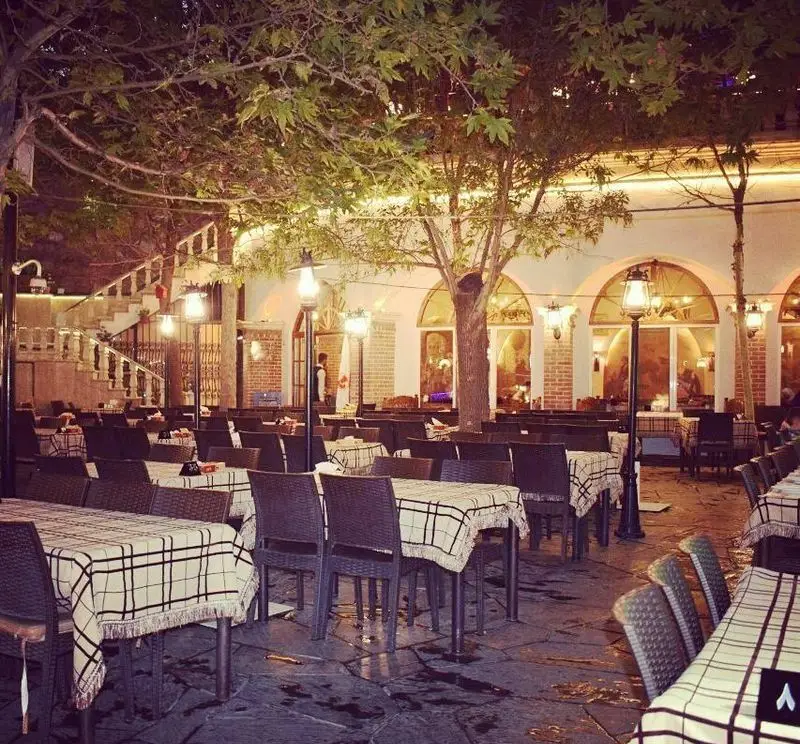تصویری دلنشین از فضای باز رستوران سفیر در شب، با چیدمان زیبا و نورپردازی گرم، میز و صندلی‌های سنتی زیر درختان.