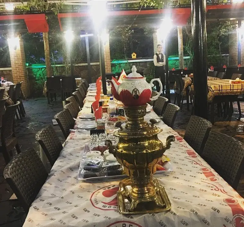 میز بلند چیده شده در فضای باز رستوران سفیر، با سماور سنتی آماده پذیرایی چای برای میهمانی‌ها و دورهمی‌های شبانه.