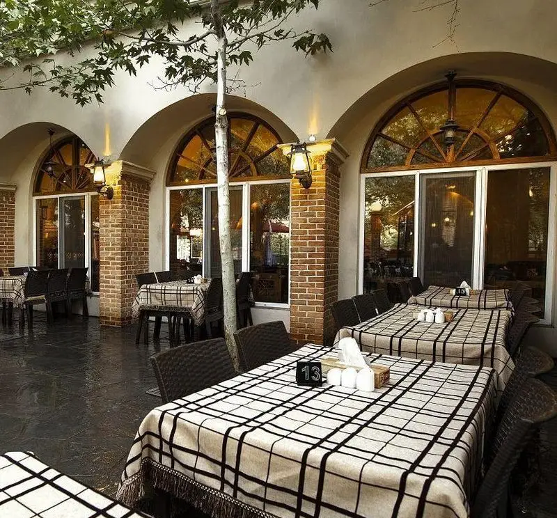 فضای باز دلنشین رستوران سفیر، با میزهای آراسته رومیزی شطرنجی، صندلی‌های حصیری و بنایی با طاق‌های آجری. مکانی عالی برای صرف غذا.