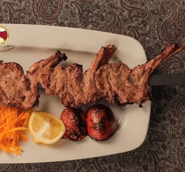 تصویر شیشلیک ویژه رستوران سفیر، کباب دنده گوسفندی آبدار با گوجه کبابی، لیمو ترش و هویج تازه، سرو شده روی سینی سفید.