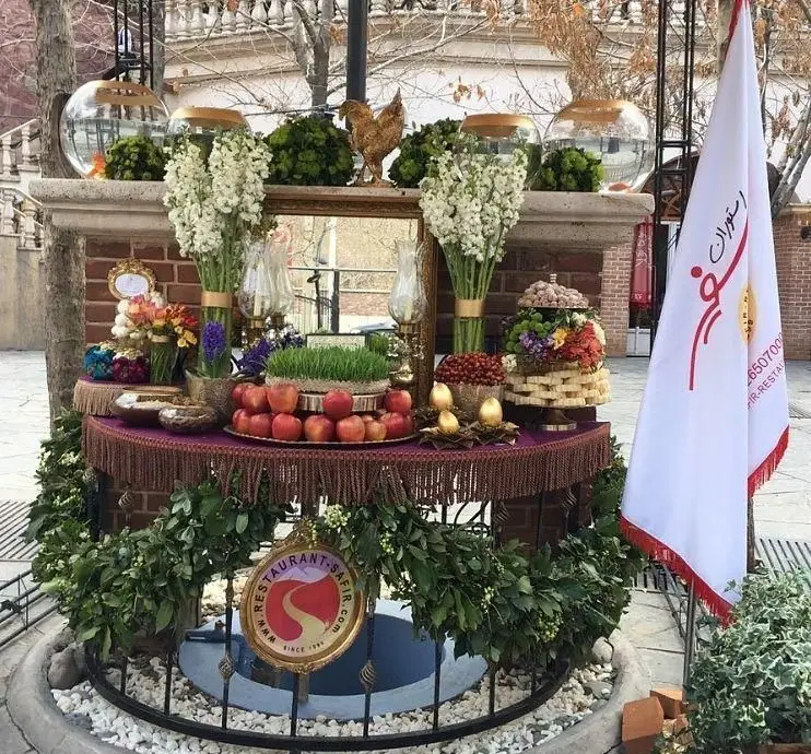میز هفت سین باشکوه رستوران سفیر برای نوروز، شامل سیب، سبزه، گل‌های تازه، تنگ ماهی و دیگر نمادهای سال نو. محیطی دلپذیر.