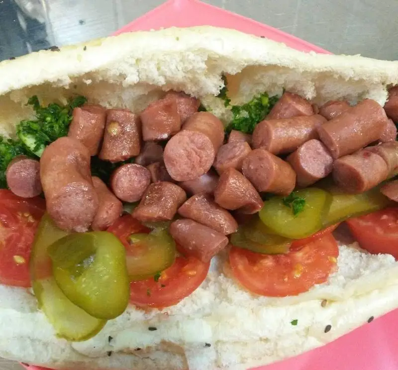 ساندویچ سوسیس مجلسی برگر هاکوپیان؛ ترکیبی دلپذیر از تکه‌های سوسیس سرخ‌شده، گوجه تازه، خیارشور و سبزی معطر داخل نان.