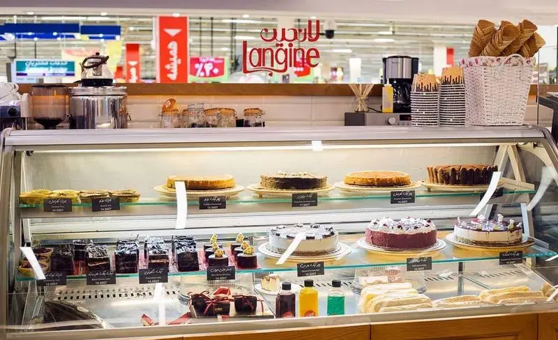 نمای داخلی کافه و رستوران لانجین با ویترینی چشم‌نواز شامل انواع کیک، شیرینی و دسرهای تازه و خوشمزه برای مشتریان.