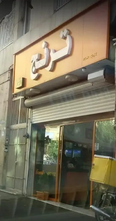 نمای جلوی پیتزافروشی ترنج با تابلوی نام مغازه و شیشه‌های ورودی، همراه با موتورسیکلت دارای جعبه تحویل غذا، نشان دهنده سرویس دلیوری.