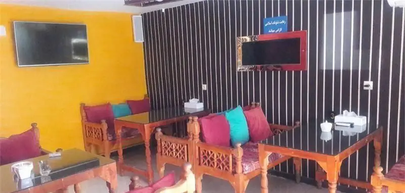 تصویری از فضای داخلی کافه سفره خانه فارا، شامل مبلمان چوبی سنتی با کوسن‌های رنگی، میزهای شیشه‌ای و تلویزیون روی دیوار راه راه. فضایی دلنشین برای مشتریان.