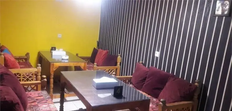 کافه سفره خانه فارا: فضای داخلی دنج با دکوراسیون سنتی ایرانی، مبلمان چوبی، کوسن‌های قرمز و میزهای شیشه‌ای، محیطی آرامش‌بخش.