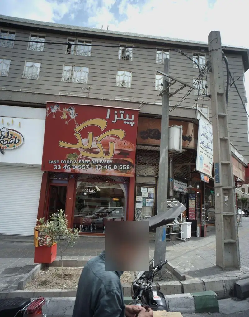 تصویر تابلوی قرمز پیتزا لک لک، فست فود و تحویل رایگان با شماره تماس 33460557 و 33460558 در خیابان.