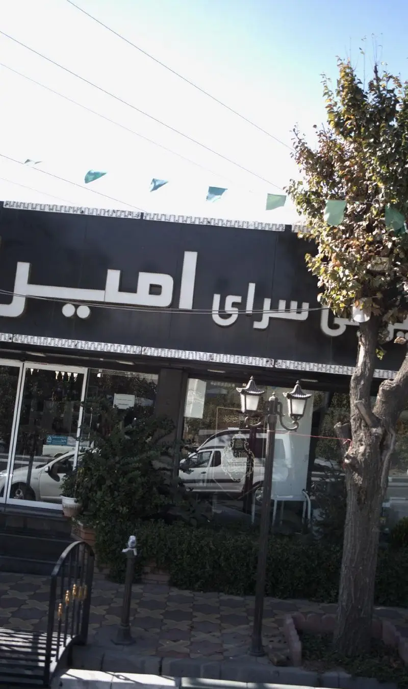 نمای خارجی شیرینی سرای امیران، یک فروشگاه قنادی مدرن با تابلوی مشکی بزرگ، ویترین‌های شیشه‌ای و فضای سبز جلویی.
