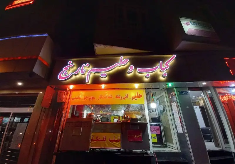 رستوران کباب و حلیم نارنج: تابلوی درخشان نئونی "کباب و حلیم نارنج" و منوی آش، حلیم، شله قلمکار و سوپ در شب.