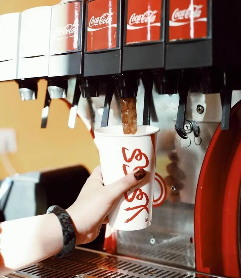 مشتری در فست فود اُ ...اینو! در حال پر کردن نوشابه از دستگاه سلف سرویس کوکاکولا با لیوان مخصوص و لوگوی اختصاصی رستوران.
