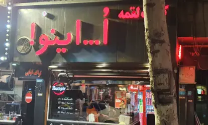 تصویری از نمای بیرونی فست فود "اُ ...اینو!" در شب با تابلوهای نئونی صورتی، ارائه دهنده لقمه، همبرگر، ساندویچ و کمپیر.