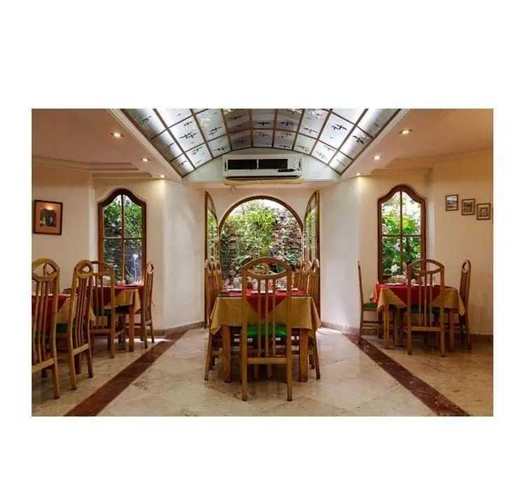 دکوراسیون داخلی رستوران قناری: فضایی دلباز با میز و صندلی های چوبی، سقف نورگیر و پنجره های قوسی شکل مشرف به طبیعت.