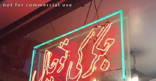 تابلوی نئون چشمگیر و رنگارنگ رستوران ایرانی جگرکی توچال با خطوط قرمز روشن و لبه های آبی درخشان، نمای داخلی.