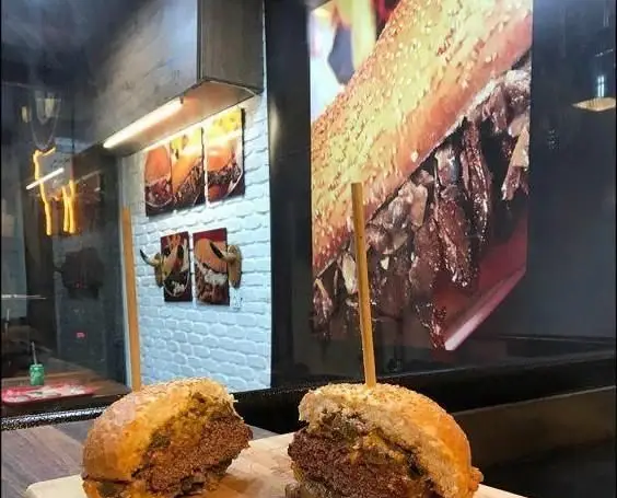 فضای داخلی رستوران برگر مستر استیک با دکوراسیون دیوارهای آجری سفید، تابلوهای همبرگر و شاخ گاو. یک برگر نصف شده خوشمزه در پیش زمینه.