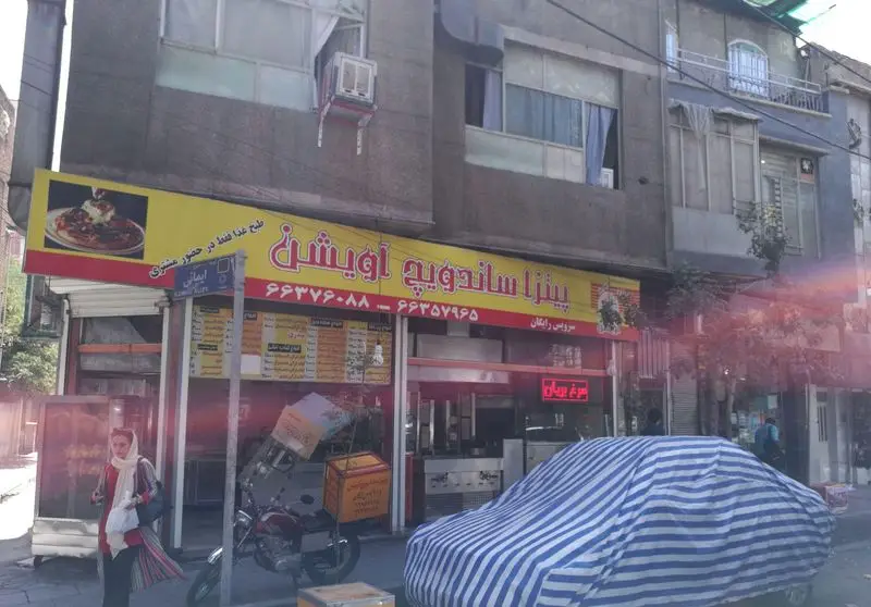 تصویر نمای خیابانی پیتزا ساندویچ آویشن: تابلوی زرد و قرمز، شماره تماس، سرویس رایگان، طبخ غذا در حضور مشتری، خیابان ایمانی تهران.