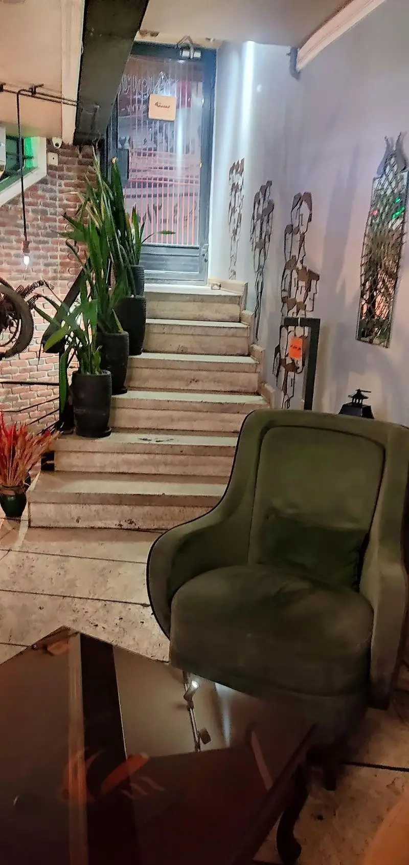 فضای داخلی دنج کافه رستوران هوکر با پله های سنگی، گلدان ها، مبلمان راحتی سبز و دکوراسیون دیوار هنری خاص