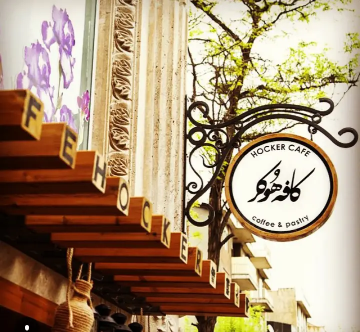 تصویر نمای بیرونی دکوراسیون کافه رستوران هوکر، شامل تابلوی آویز HOCKER CAFE و حروف چوبی نام کافه، مناسب برای قهوه و شیرینی.