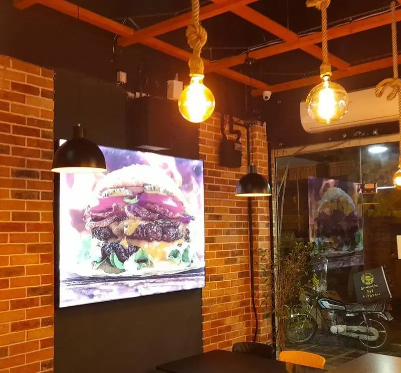 دکوراسیون داخلی فست فود پیتزا ساندویچ ورنا با دیوارهای آجری، نورپردازی خلاقانه، و تابلوهای نورانی برگرهای ویژه.