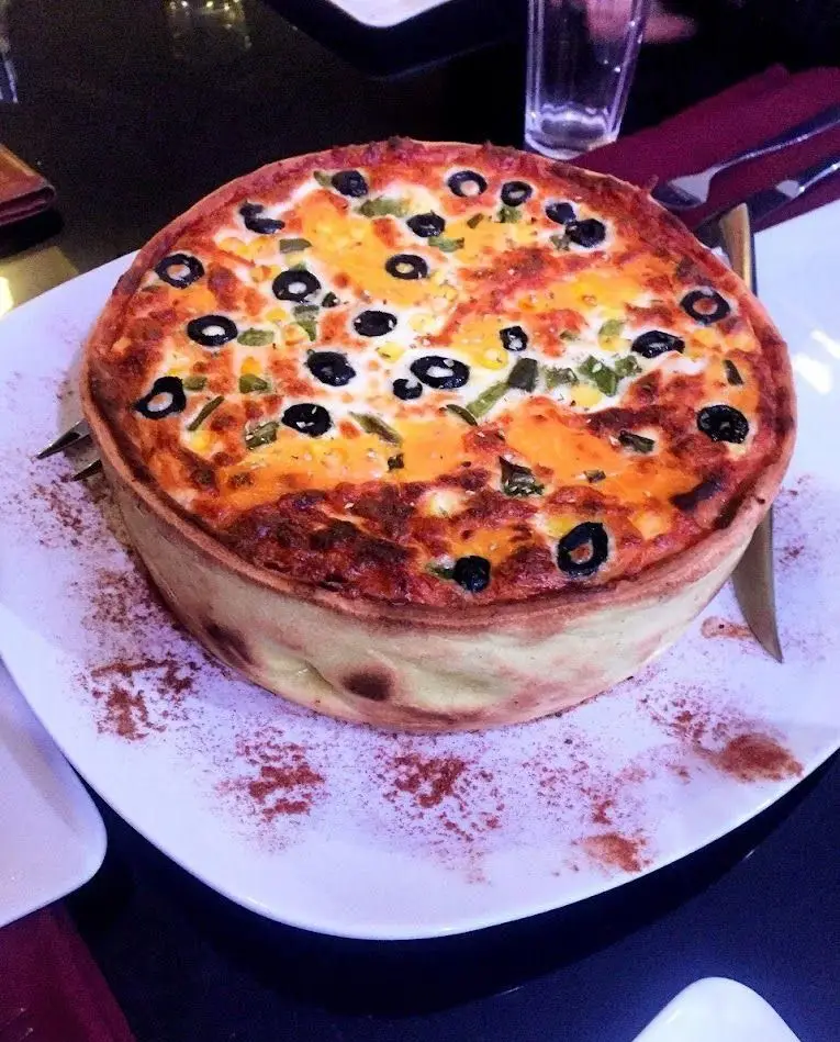 تصویری جذاب از کیش یا تارت عمیق رستوران آروما با پنیر، زیتون و فلفل، انتخابی لذیذ برای تجربه غذایی منحصر به فرد.