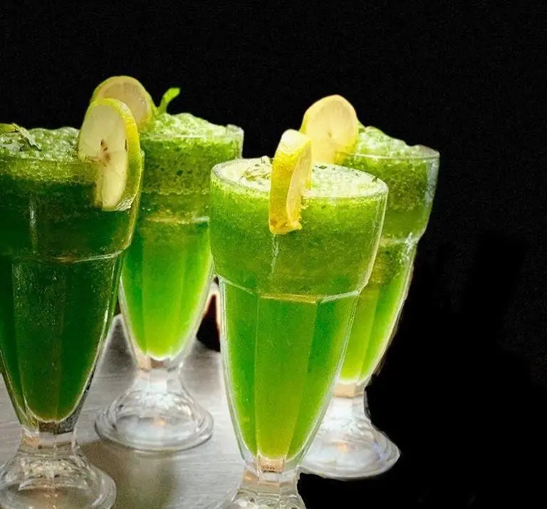 چهار لیوان نوشیدنی موهیتو خنک و گوارا با رنگ سبز دلنشین و برش‌های لیموی تازه، انتخابی عالی در پیتزا نایت.