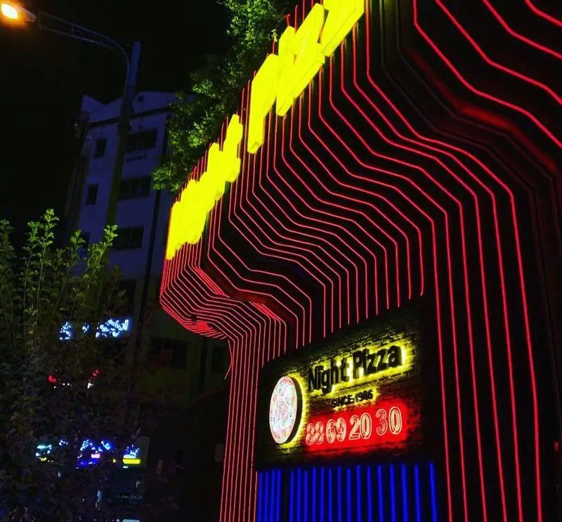 تابلوی پرنور پیتزا نایت در تاریکی شب با چراغ‌های نئون قرمز و زرد، شامل لوگو پیتزا، عبارت 'Since 1986' و شماره تلفن ۸۸۶۹۲۰۳۰.