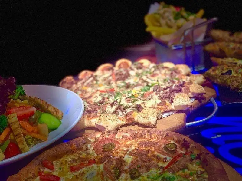 میز شلوغ پیتزا نایت با دو پیتزای پرطرفدار و خوش‌طعم، یک کاسه سالاد تازه و سبزیجات متنوع، به همراه سیب زمینی سرخ‌کرده داغ.