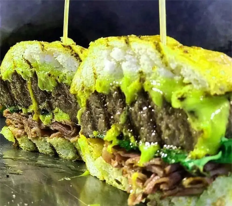 ساندویچ برگر دیزلی با نان سبز خاص و سس آووکادو، برش خورده و آماده سرو. تجربه‌ای خوشمزه از فست فودهای باکیفیت.