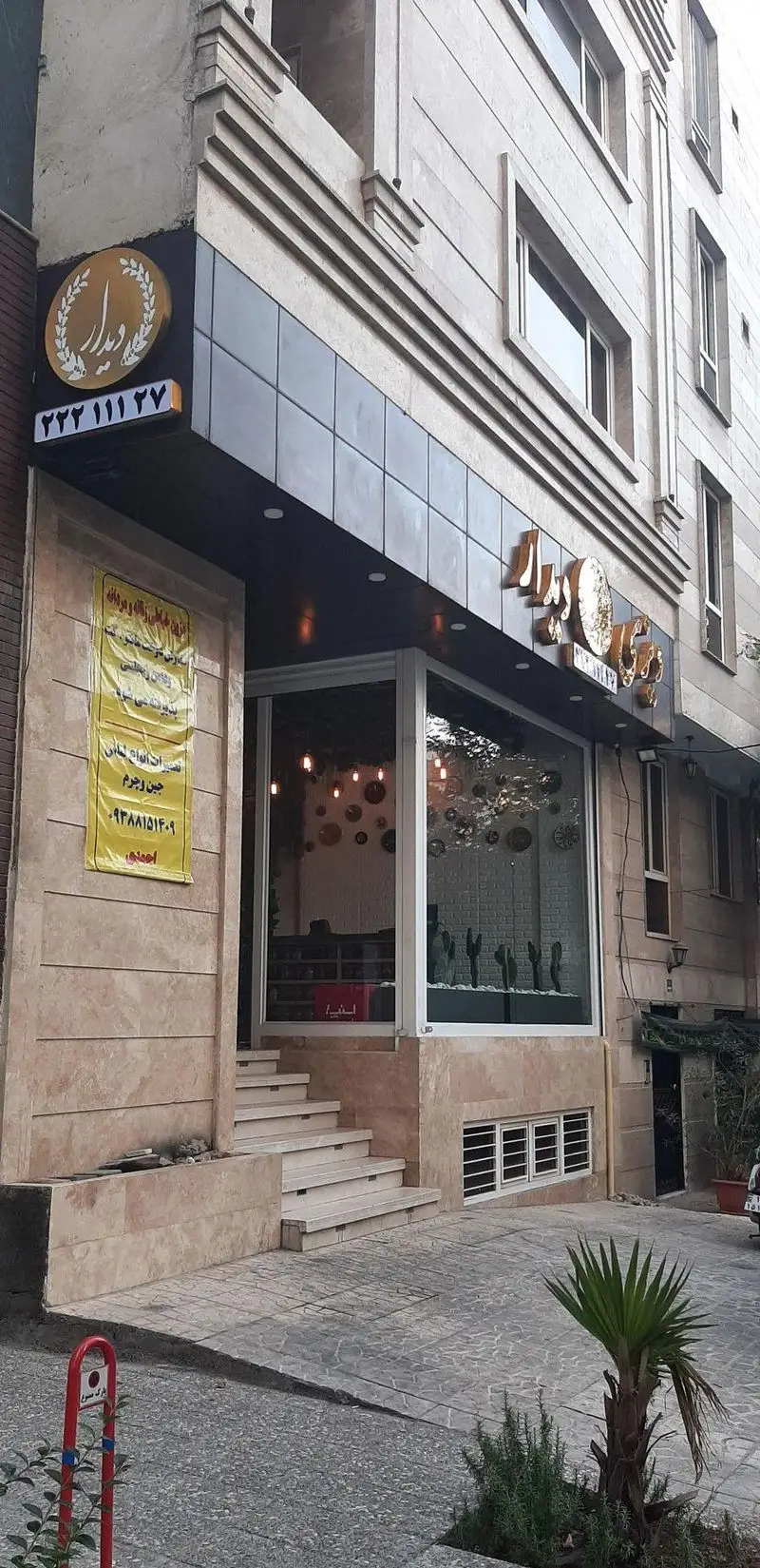 نمای ورودی رستوران دیزی دیدار با تابلوی جذاب طلایی رنگ و شماره تماس، پله‌های سنگی و پنجره‌های بزرگ، فضایی دلنشین برای صرف دیزی.