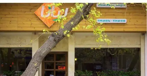 نمای بیرونی جذاب رستوران ایتالیایی لیانا با تابلوی نام، منوی پیتزا، پاستا، برگر و شماره تماس‌ها روی دیوار چوبی، همراه با درخت.