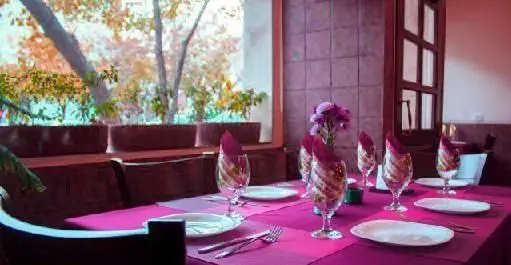 محیط دنج و زیبای رستوران ایتالیایی لیانا با میزهای آماده، دکوراسیون صورتی-بنفش و منظره تماشایی درختان پاییزی.