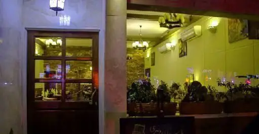 نمایی از ورودی شیک و دلنشین رستوران ایتالیایی لیانا، با درب چوبی و بازتاب فضای داخلی گرم و نورانی آن در شب.