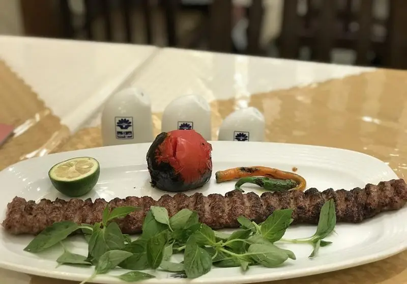 کباب کوبیده اصیل و پرطرفدار چلوکبابی ضیافت، با گوجه کبابی، لیمو ترش و سبزی تازه در محیط رستوران.