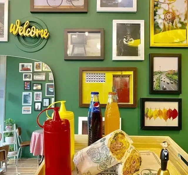 دکوراسیون شیک ساندویچی باماهاس با دیوار سبز چشم‌نواز، ساندویچ‌های لذیذ، نوشیدنی‌های خنک و محیطی جذاب برای مشتریان.