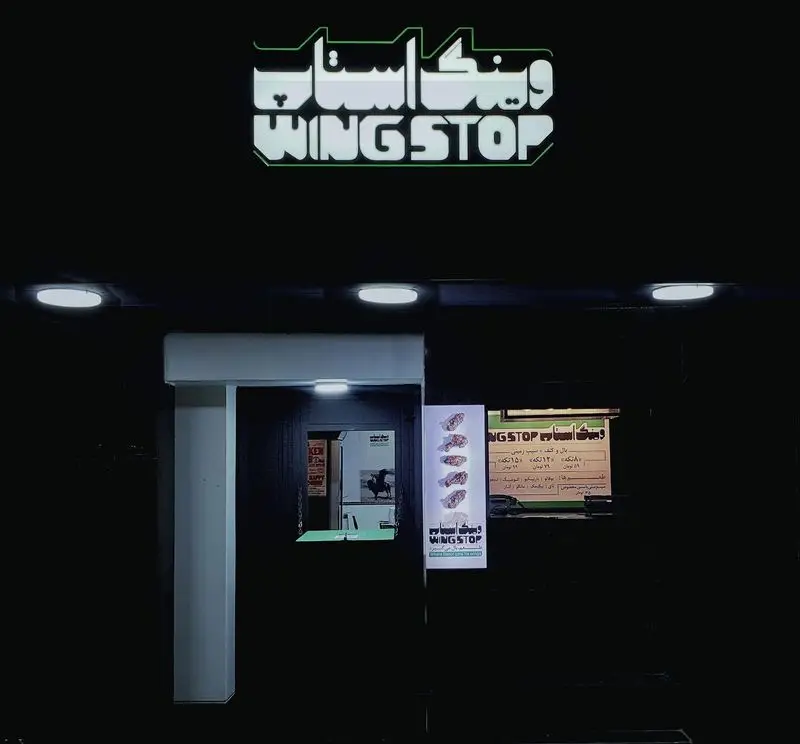 نمای بیرونی رستوران وینگ استاپ در شب با لوگوی درخشان و تابلوهای تبلیغاتی غذاهای خوشمزه مرغ و بال.