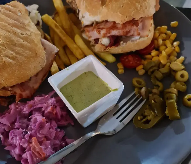 بشقاب لذیذ کافه هومان: ساندویچ‌های دلچسب، سیب زمینی سرخ کرده، سالاد کلم بنفش، سس سبز، ذرت، زیتون و فلفل هالوپینو.