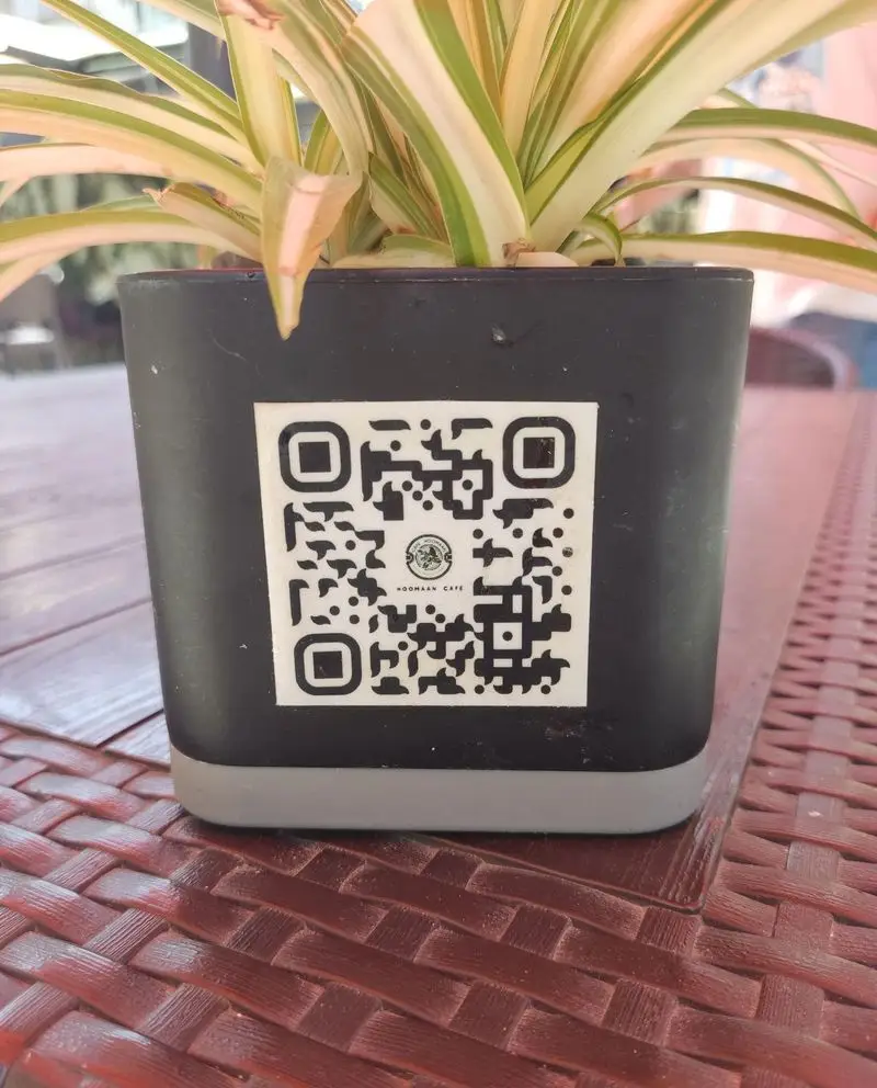 QR کد کافه هومان روی گلدان میز رستوران برای دسترسی سریع به منو و سفارش آنلاین قهوه و غذا. تجربه راحت در کافه.