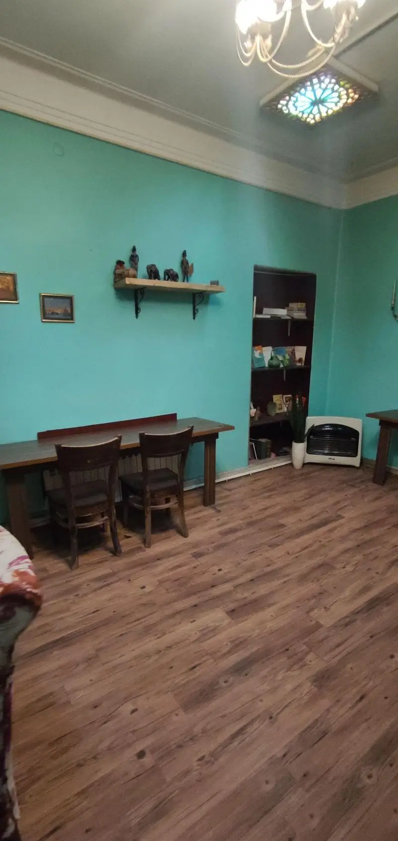 فضای داخلی دنج و دلنشین کافه حوض کاشی با دیوارهای فیروزه‌ای، کفپوش چوبی، میز و صندلی‌های قهوه‌ای و تزئینات هنری.