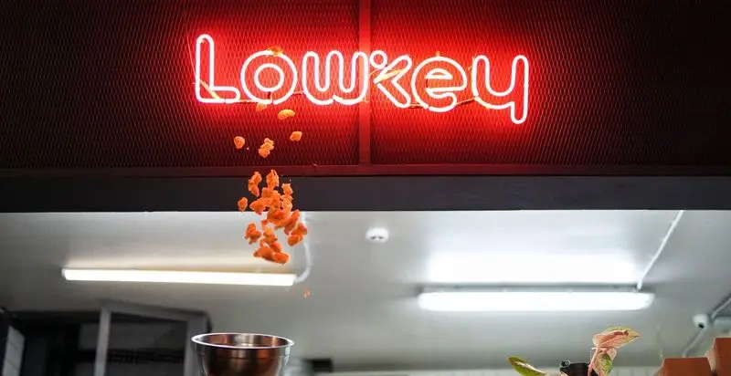 نمای داخلی کافه رستوران لوکی با تابلوی نئون "Lowkey" و سرو هیجان‌انگیز غذا، نشان‌دهنده فضای مدرن و پویا.