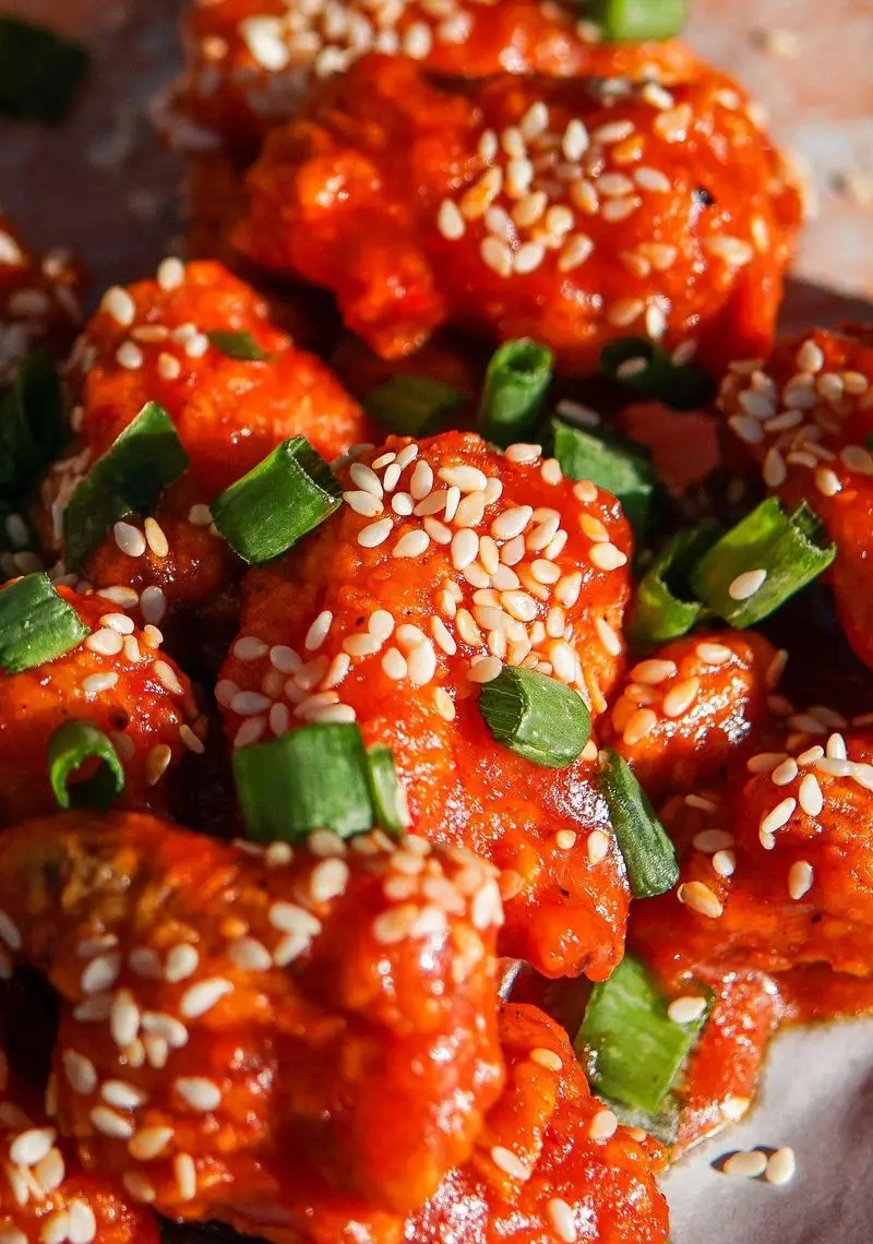 مرغ‌های ترد و آبدار با روکش سس قرمز براق، کنجد فراوان و پیازچه خرد شده، آماده سرو در کافه رستوران لوکی.