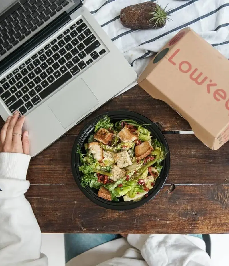سالاد تازه و سالم لوکی برای ناهار کاری، سفارش بیرون‌بر کافه رستوران لوکی کنار لپ‌تاپ روی میز چوبی.