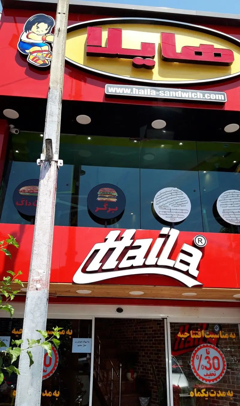 نمای بیرونی فست فود هایلا با لوگو، تابلو، آدرس سایت haila-sandwich.com و آگهی استخدام پیک، همراه با تخفیف ویژه افتتاحیه.