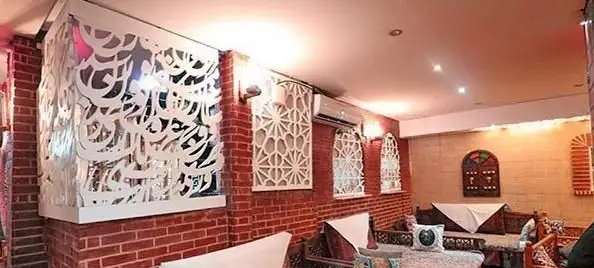 محیط دنج و سنتی کافی شاپ دلنوازان با دیوارهای آجری، کتیبه‌های خطاطی فارسی و دکوراسیون اصیل ایرانی، ایده‌آل برای استراحت.