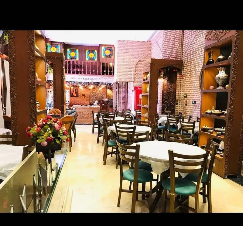 دکوراسیون داخلی گرم و سنتی سفره خانه گوهرانه با میز و صندلی چوبی، دیوارهای آجری، قفسه‌های تزئینی و فضایی دلنشین برای مشتریان.