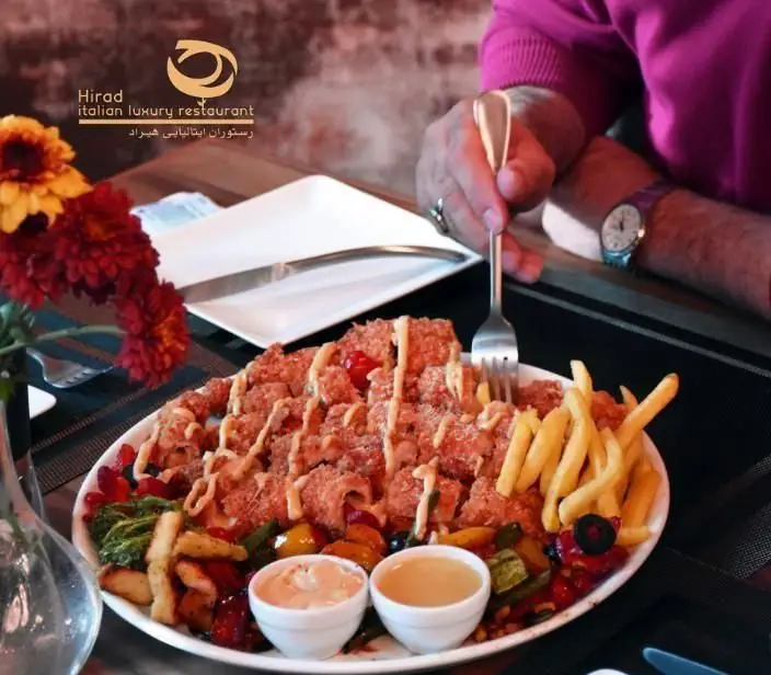 تصویری جذاب از یک غذای کامل شامل مرغ سوخاری، سیب زمینی و سبزیجات تازه در رستوران ایتالیایی لوکس هیراد، برای تجربه‌ای دلپذیر.