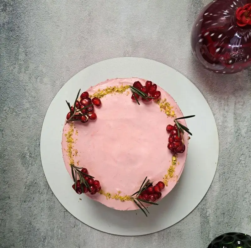 کیک زیبای صورتی لونا کیک با تزیین هنرمندانه انار، رزماری تازه و خرده پسته. دسر عالی برای جشن ها و رویدادهای شما.