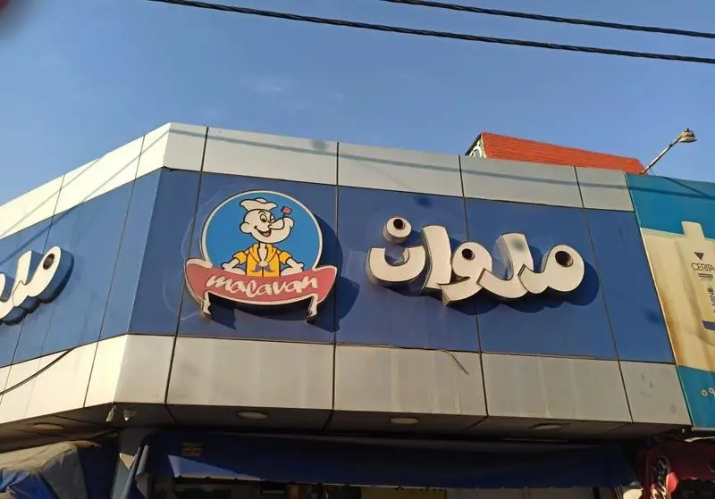 تابلوی فست فود ملوان با لوگوی جذاب شخصیت ملوان کارتونی (شبیه ملوان زبل) با کلاه سرآشپز روی نمای آبی. بهترین انتخاب برای غذای سریع و خوشمزه.