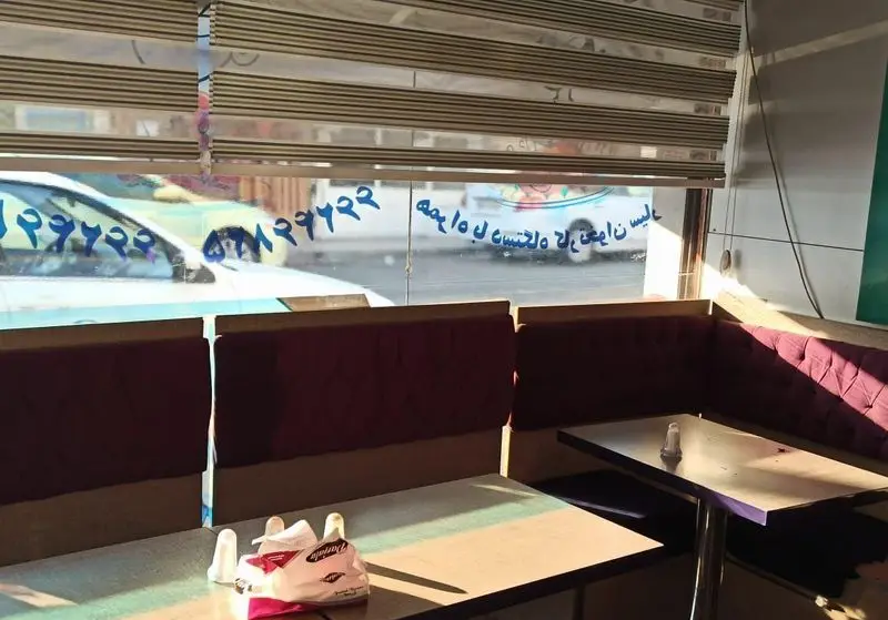 تصویری از فضای دلنشین و تمیز فست فود ملوان، شامل میز و نیمکت‌های راحت قرمز رنگ کنار پنجره با نور طبیعی خورشید.