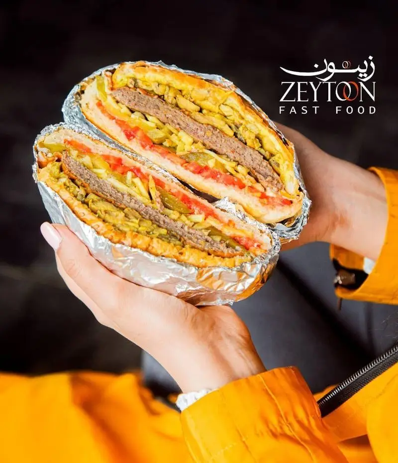 ساندویچ غول‌پیکر و خوشمزه رستوران فست فود زیتون با محتویات برگر، سیب‌زمینی و سبزیجات تازه، پیچیده در فویل آماده برای لذت بردن.